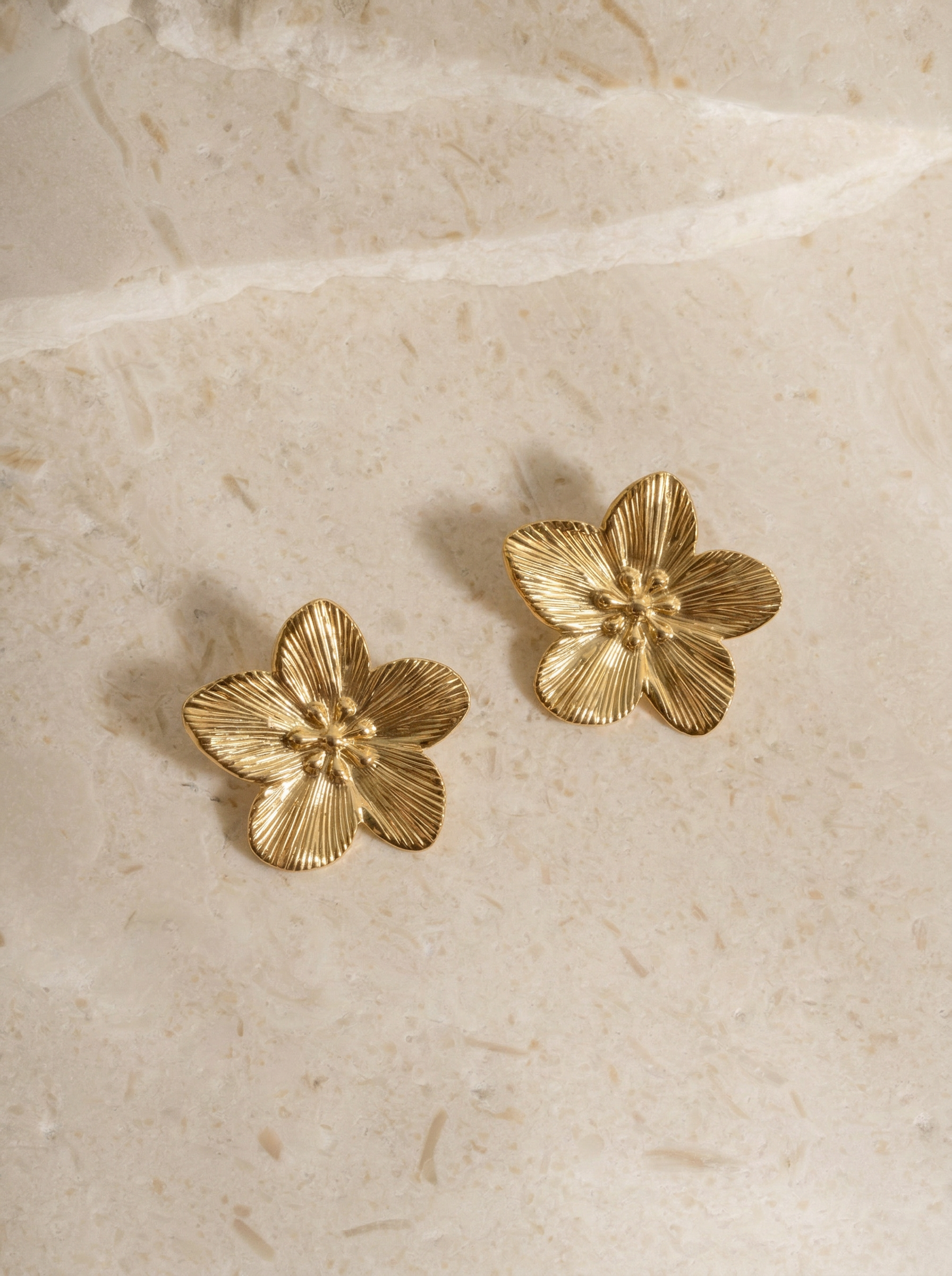 golden_flower_earrings_on_stone_surface.png