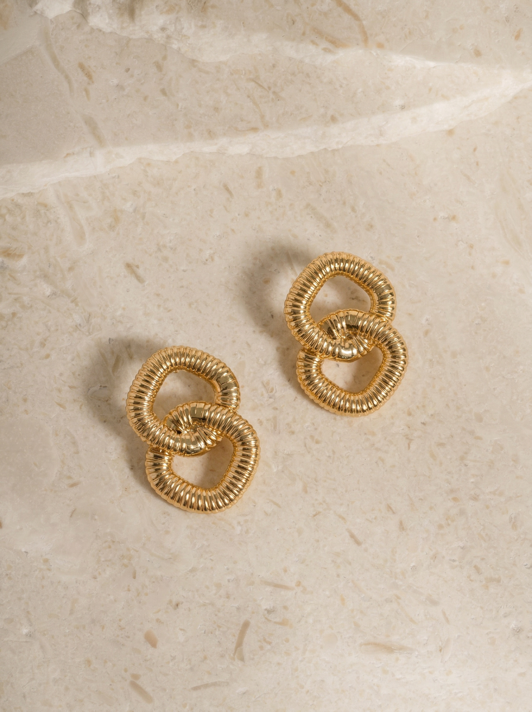 interlocking_gold_square-loop_earrings_on_beige_background.png
