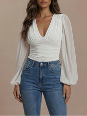 Woman wearing a white blouse with sheer sleeves and blue jeans on a beige background